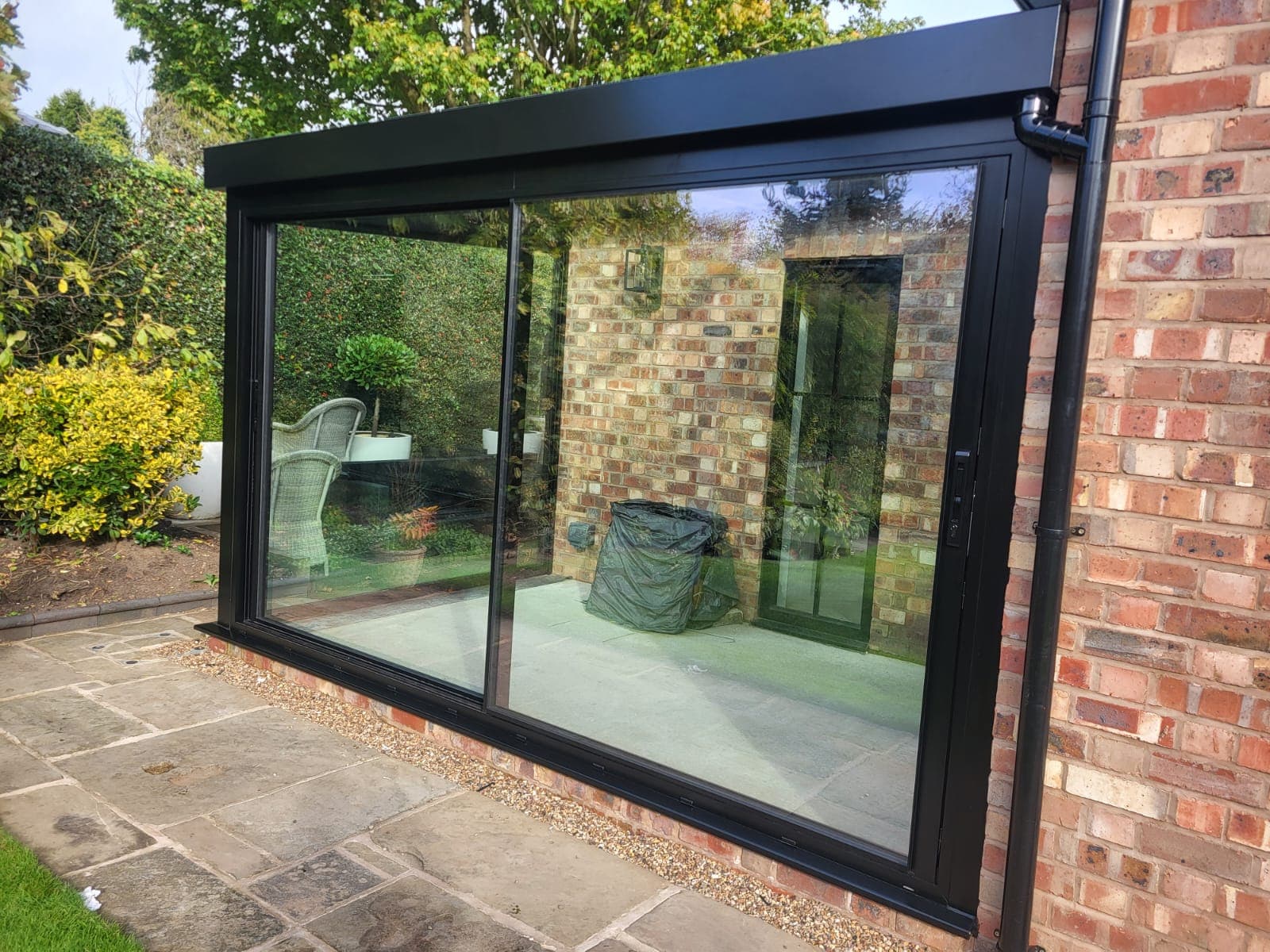Black-framed glass box with wide sliding doors and glass roof against brick in Bowdon, Cheshire